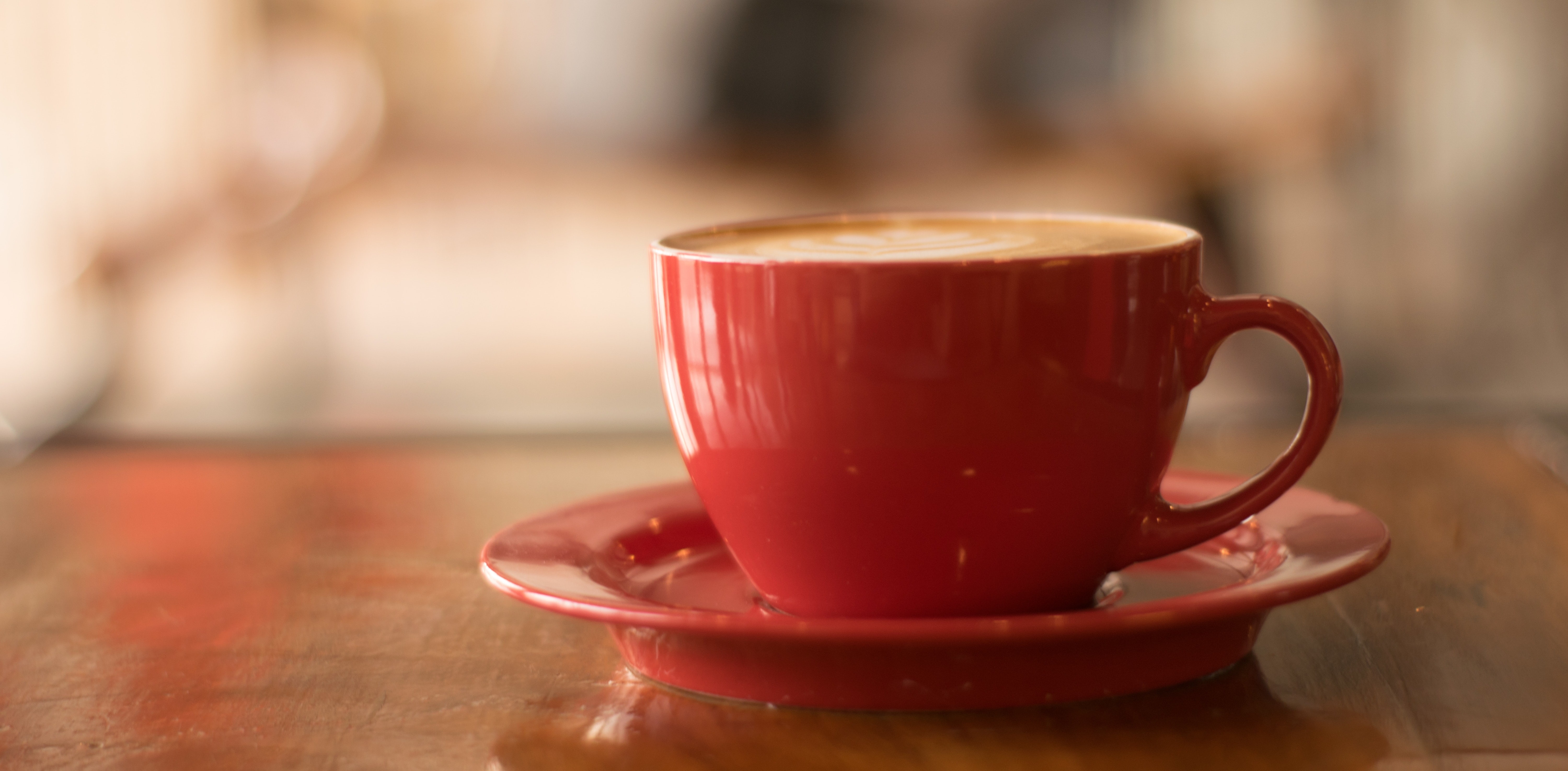Red coffee cup, sitting on red saucer and filled with coffee.